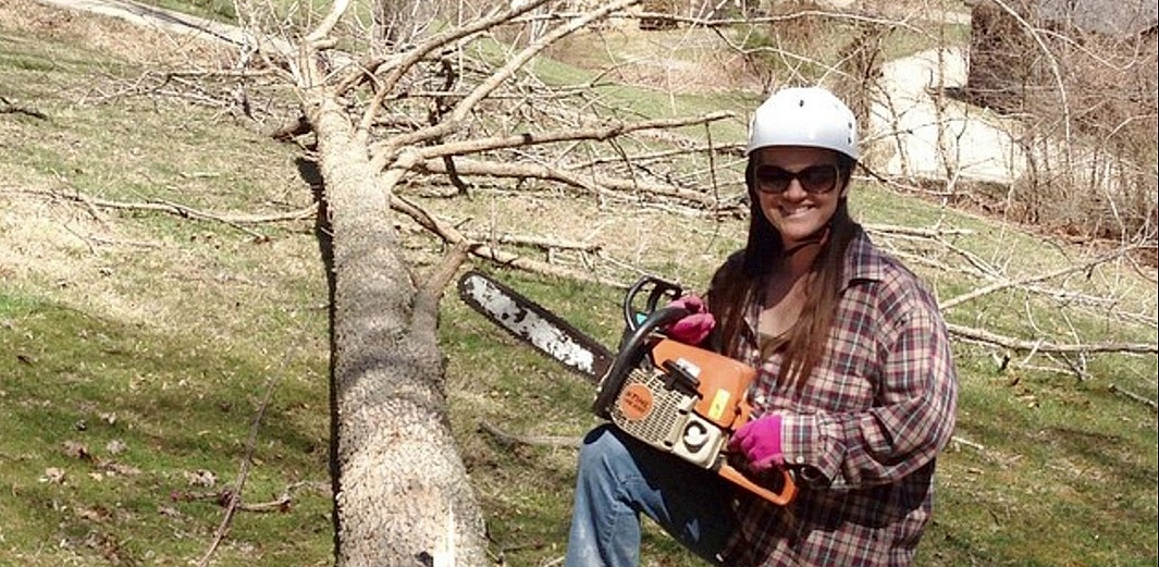 Co-Owner and Grounds Girl standing with chainsaw and PPE.